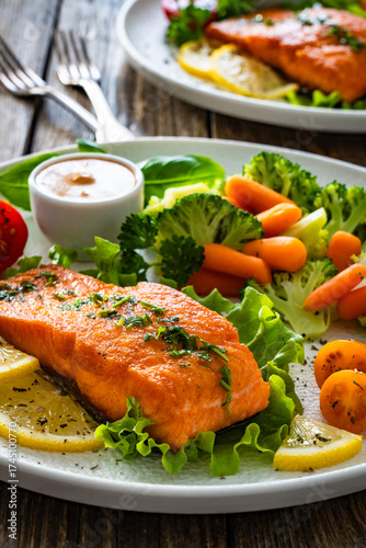 Fried salmon steak with boiled broccoli and mini carrots and sauce on wooden table	