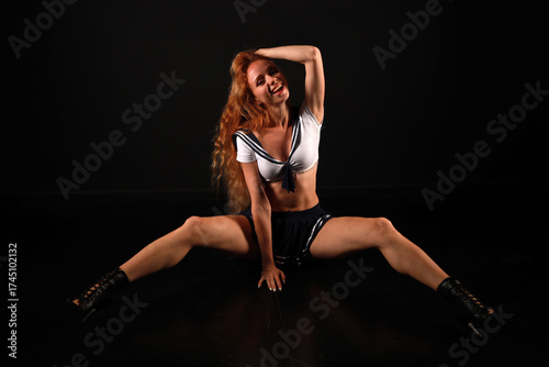 A red-haired long-legged girl in a sailor costume sitting on the floor in a half-split low key portrait