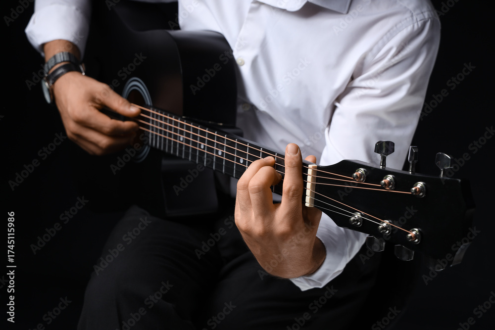 Fototapeta premium Young man playing guitar on black background