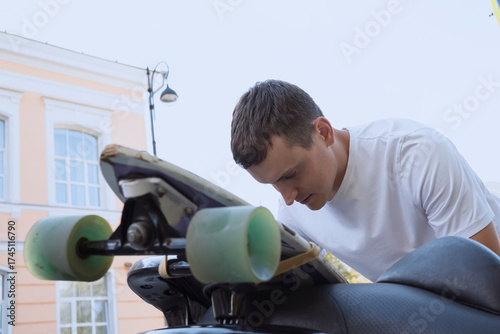 man attaching skateboard to motorbike outdoors in city