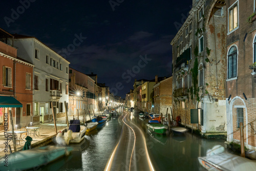 Venetian canal at night with boats and historic buildings.