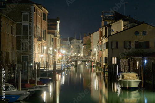 Venetian canal at night with illuminated reflections.