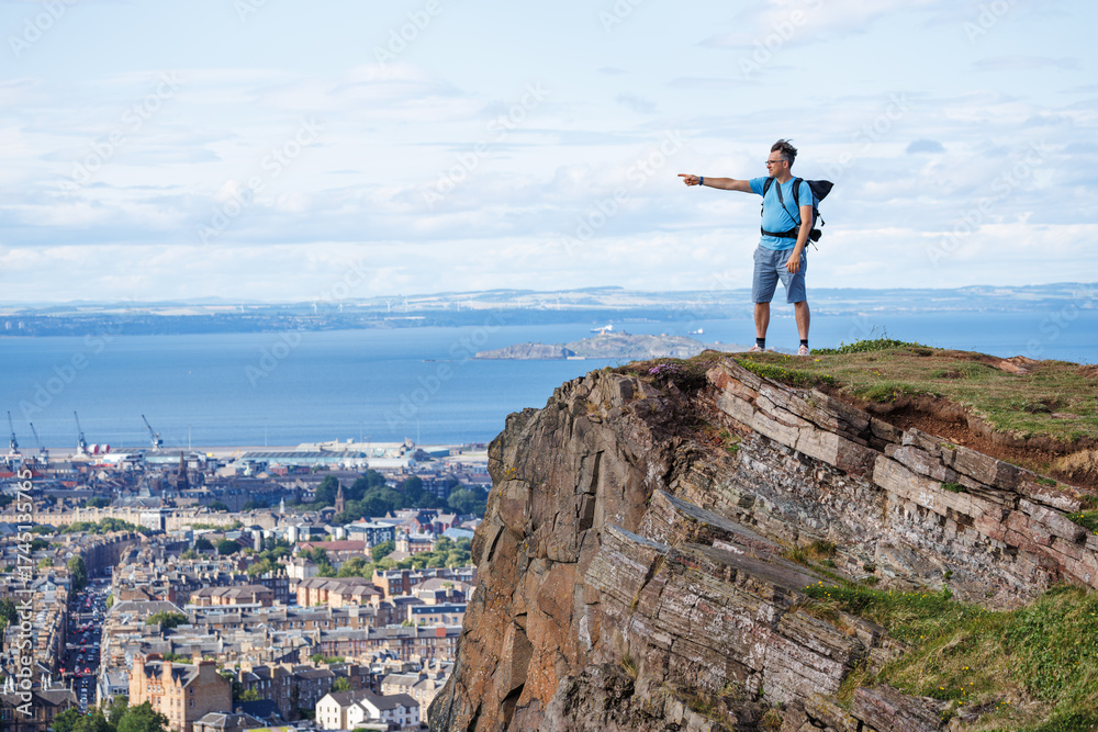 Obraz premium Hiker points from high cliff, viewing cityscape and ocean scene