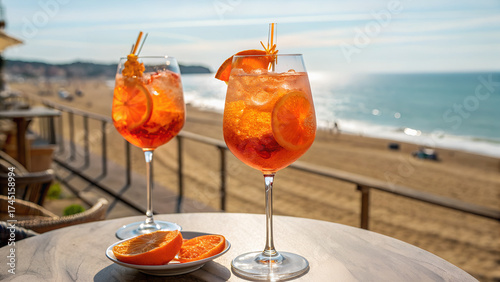 Two glasses of orange spritz aperol drink cocktail on the table outdoors summer sunny day with sea and beach view blurred background.