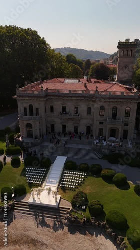 Aerial drone view of historic Villa Erba on Lake Como with bell tower, floral arch, and semicircle rows of chairs set for luxury destination wedding overlooking the scenic lake and mountains