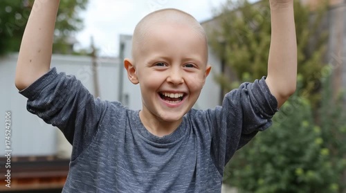 Smiling bald child raising hands in victory