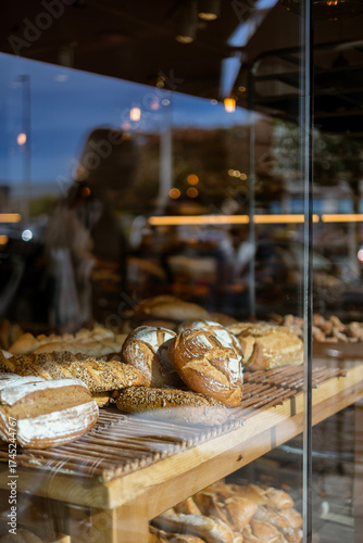 A display window of a local bakery or cafe, filled with fresh artisanal bread. Reflections of the city street are on the glass, a concept of small business and traditional baking.