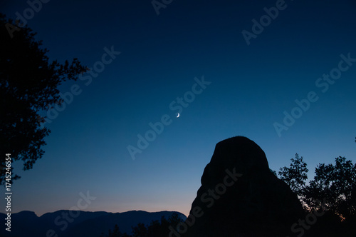 Sliver of moon above ark dark woods and hills