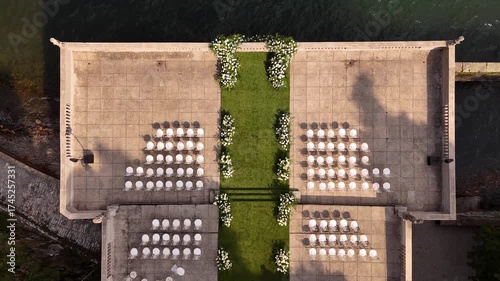 Drone aerial view of Villa Pizzo terrace on Lake Como decorated for luxury wedding ceremony with floral arch and elegant rows of chairs overlooking the scenic water and mountains