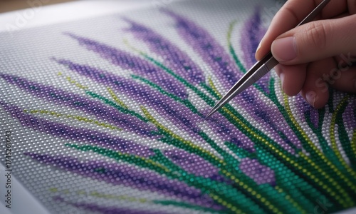 Close-up of a diamond painting in progress. Tweezers place crystals onto a lavender flower design