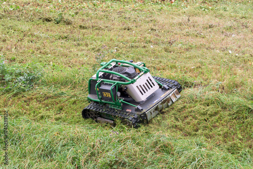 Remote-controlled tracked mower navigates tall grass, showcasing smart landscape care technology for efficient and safe maintenance.