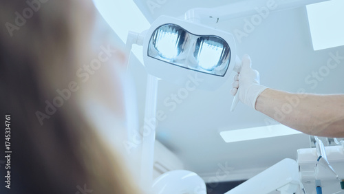 Fotografie A dental professional, wearing gloves, holds a bright dental light, illuminating a patient's mouth in a clean, well-lit office