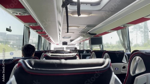 Interior view of a modern long-distance coach bus with empty seats and a few passengers. Overhead