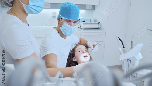 A dentist examines a young patient in a modern, clean dental office. Both wear protective gear, emphasizing hygiene and safety.