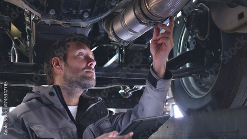 A mechanic examines a car's exhaust system with a tablet in a well-lit auto shop, emphasizing precision and detail.