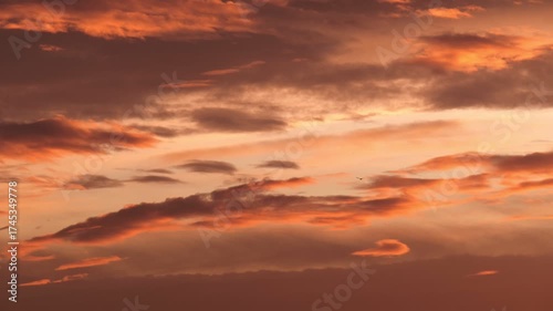 A vibrant sunset with orange and pink hues illuminating the sky. Wispy clouds create a dramatic effect against the colorful backdrop.