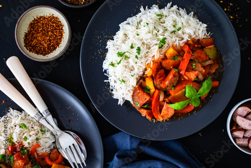 Polish lecho with white rice - bell pepper tomato stew with sausages on black table. Top view