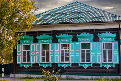 Facade of an old wooden logs house with row of windows and carved frames. Turquoise and white open shutters decorate the historic house, Russia.