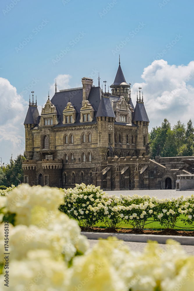 Obraz premium Majestic historic mansion surrounded by blooming flowers on a sunny day with blue skies