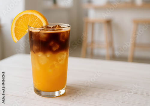 Bumble coffee refreshing beverage in a glass filled with orange juice and ice and topped with a dark espresso layer on a wooden table of modern cafe.