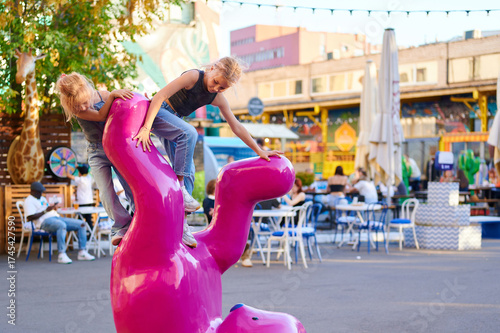 Children playing on pink bear sculpture in urban plaza