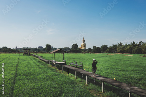 Summer travel holiday vacation concept Traveler asian woman traveling on rice​ field farm with big golden buddha statue at Wat Muang Temple in Ang Thong Thailand