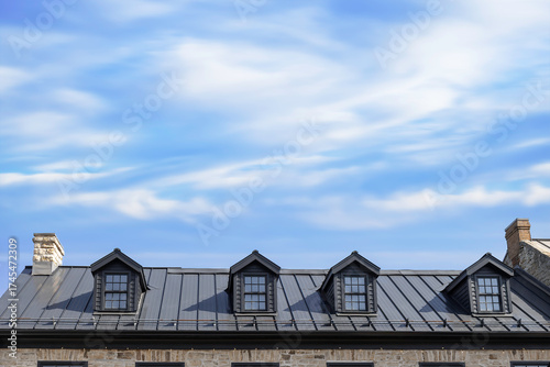 A brown metal roof with four dormer windows, stone chimneys, blue sky with clouds, sunshine, nobody