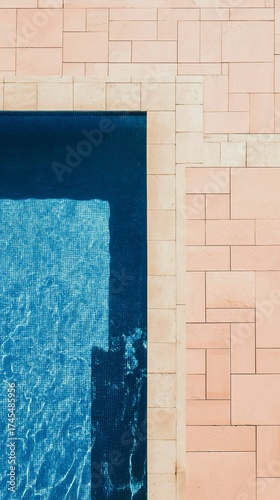 Vista dall'alto di un angolo di piscina. L'acqua è di un blu intenso con riflessi chiari dovuti alla luce del sole. Il bordo della piscina è circondato da piastrelle di colore rosa chiaro 