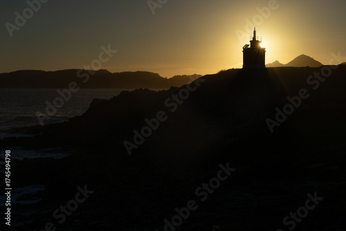 Punta Robaleira red lighthouse in Home cape at sunset in Rias Baixas zone in Galicia coast with Cíes islands in the background.