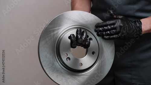 Close-up of gloved auto mechanic holding new, high-quality brake disc, running hand over it. Concept of auto parts replacement, vehicle brake system maintenance, safety