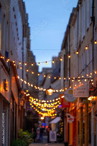 Obraz na plátně Narrow Shopping street with lights strung across at dusk in England