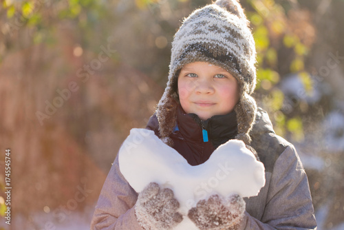 Boy enjoying peaceful winter day with snow heart, Valentine mood