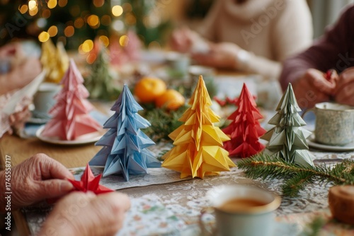 Colorful paper origami Christmas trees sit on a decorated table as people gather for a festive holiday celebration.