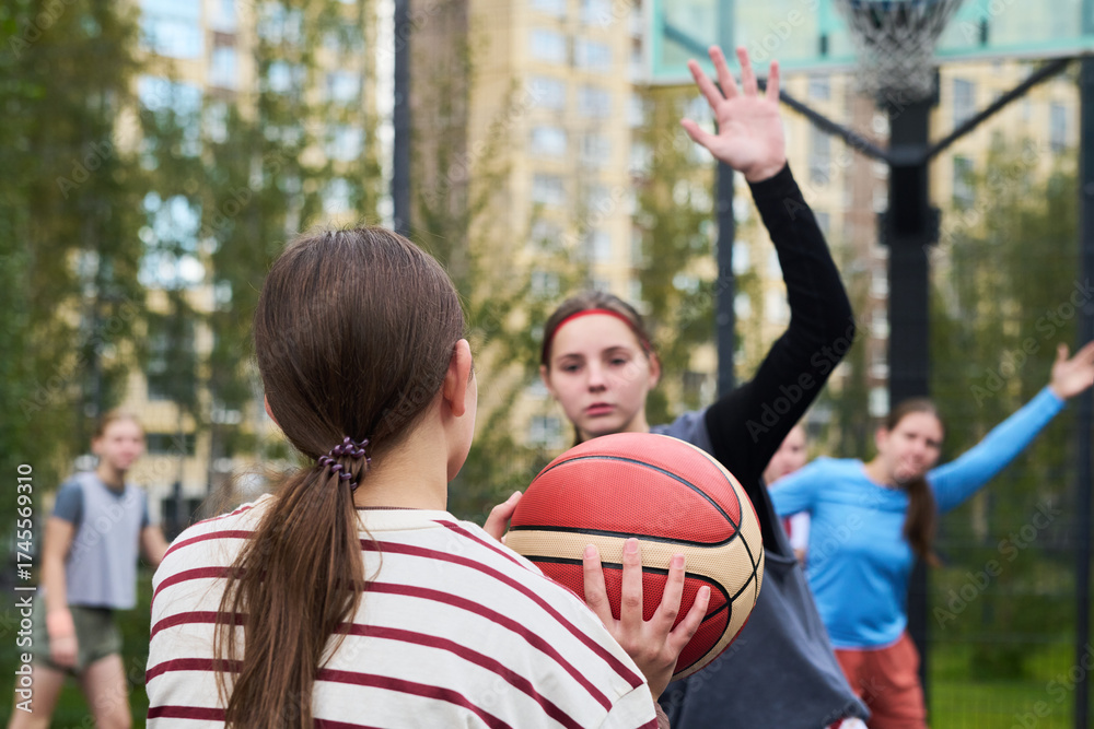 Fototapeta premium Teenage Caucasian girl holding basketball preparing to pass while another teenage Caucasian girl defending with raised arm during streetball game