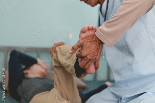 The hands of doctor or physical therapist's examine a young man with disability in a wheelchair for muscle stiffness and dyskinesia are common symptoms in people with CP or cerebral palsy.