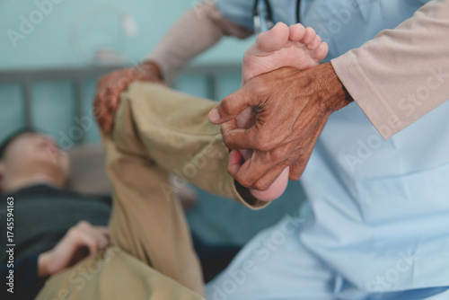 The hands of doctor or physical therapist's examine a young man with disability in a wheelchair for muscle stiffness and dyskinesia are common symptoms in people with CP or cerebral palsy.