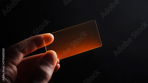 Translucent card held in hand, isolated against a black background, exhibiting a faint golden hue. Simplicity and focus on technological materials.