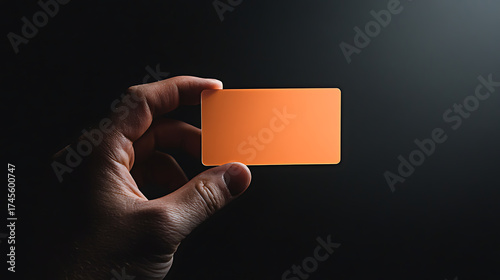 Orange card held in hand against dark background. Minimalist composition emphasizing color and shape, providing space for text or graphic overlay.