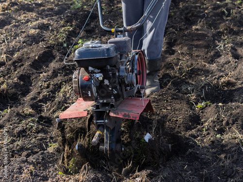 Wallpaper Mural Individual using a tiller to cultivate soil in a garden, wearing gray pants and boots, surrounded by a rustic wooden fence and freshly turned earth, showcasing gardening activity Torontodigital.ca