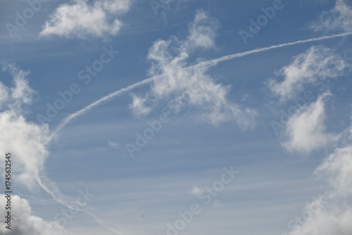 Black and white clouds on a blue sky background, chemtrail lines in the sky