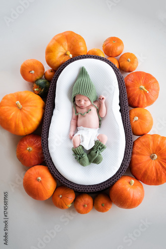 A newborn boy sleeps in a hat in a brown cradle decorated with pumpkins. Portrait of a sleeping baby on Halloween