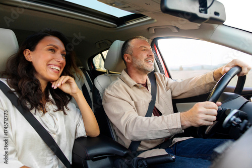 Excited European spouses going on vacation by automobile, sitting in nice brand new car, looking at road and smiling