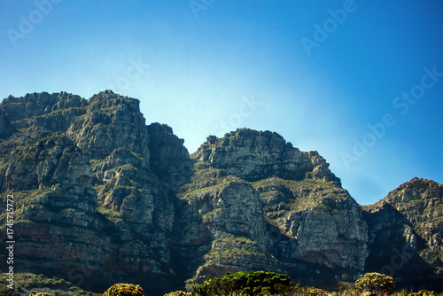 Steep rocky cliffs of Table Mountain in Cape Town, South Africa, clear blue sky. Patches of green vegetation