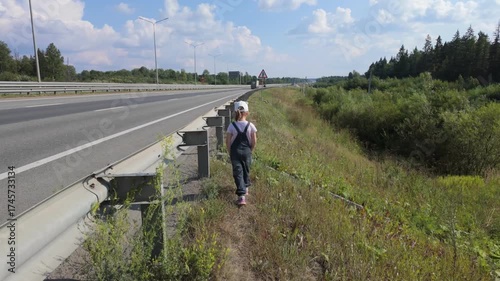 A child, a five-year-old girl, walks along the side of the highway.