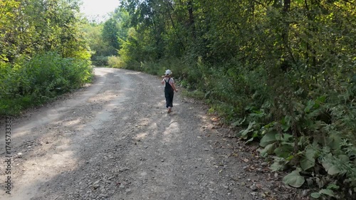 A five-year-old girl walks alone along a gravel road in the forest.