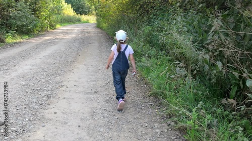 A five-year-old girl walks alone along a gravel road in the forest.