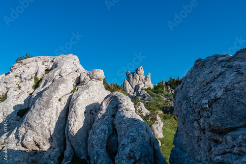 Jagged white limestone peaks rise towards a clear, deep blue sky on a sunny day. This stunning karst landscape is a famous landmark for hikers and climbers in the Velebit mountains of Croatia.