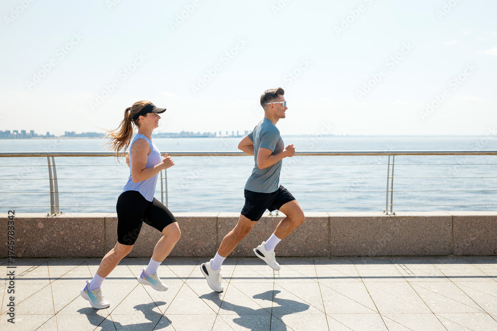 Obraz premium Couple jogging along waterfront path on sunny day near city skyline