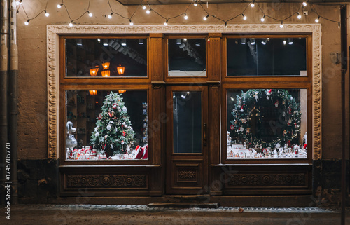 Photography A green decorative Christmas tree and a Christmas wreath stand in a illuminated storefront in Lviv