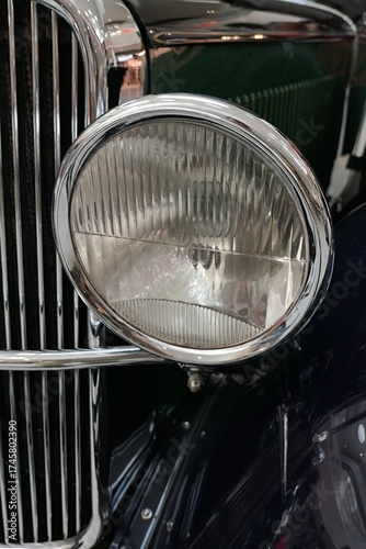 Detail off round vintage headlight in chrome frame on oldtimer Czechoslovak limousine from year 1930. Front mask chrome grille in background. 